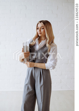 Blonde in a gray suit and white shirt holding a book standing on a white background. 118829510