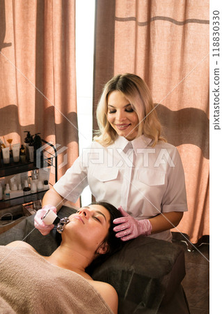 Cosmetologist performs microcurrent facial treatment 118830330