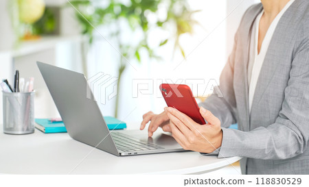 A female business person using a laptop and smartphone in the office A female business person using a laptop and smartphone in the office 118830529