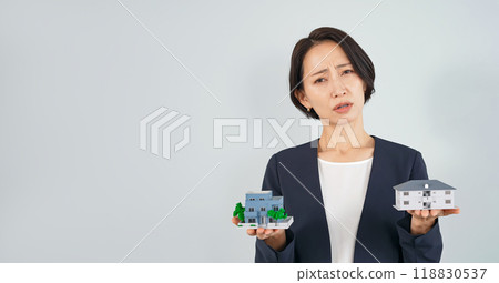 A middle-aged woman holding a house model and worrying 118830537