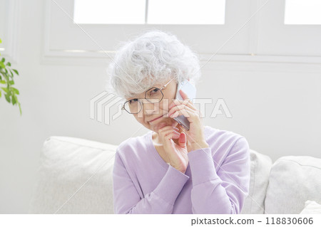 Senior woman thinking while talking on smartphone in living room Senior woman thinking while talking on smartphone in living room 118830606