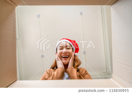 Low angle view of surprised young Asian woman wearing Christmas hat and unpacking 118830955