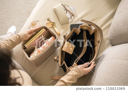 A young beautiful woman is collecting her women's bag. He puts away his diary, glasses, keys, phone A young beautiful woman is collecting her women's bag. He puts away his diary, glasses, keys, phone 118831069