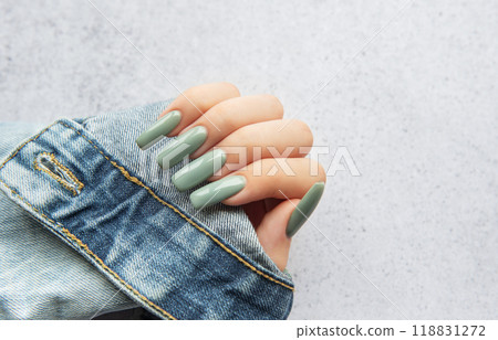 A hand with long green nails resting on a denim sleeve against a textured background 118831272