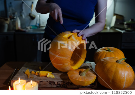 A woman is skillfully carving a pumpkin for halloween that rests on a cutting board A woman is skillfully carving a pumpkin for halloween that rests on a cutting board 118832500
