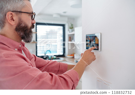 Man using smart thermostat, adjusting, lowering heating temperature at home. Concept of sustainable, efficient, and smart technology in home heating and thermostats. Man using smart thermostat, adjusting, lowering heating temperature at home. Concept of sustainable, efficient, and smart technology in home heating and thermostats. 118832732