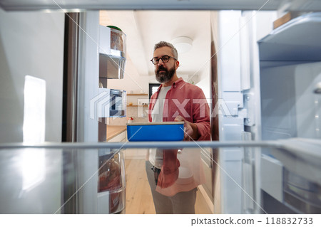 Handsome man putting lunchbox in fridge. Taking out lunch from fridge, eating leftovers. Stop trowing food away, reducting food waste. Handsome man putting lunchbox in fridge. Taking out lunch from fridge, eating leftovers. Stop trowing food away, reducting food waste. 118832733