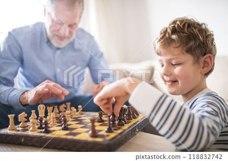 Grandpa teaching young boy to play chess. Grandfather spending time with grandson, taking care of him while parents are at work. Grandpa teaching young boy to play chess. Grandfather spending time with grandson, taking care of him while parents are at work. 118832742