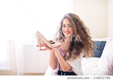 Portrait of beautiful young woman with curly hair holding pair of nude heels. Portrait of beautiful young woman with curly hair holding pair of nude heels. 118832786