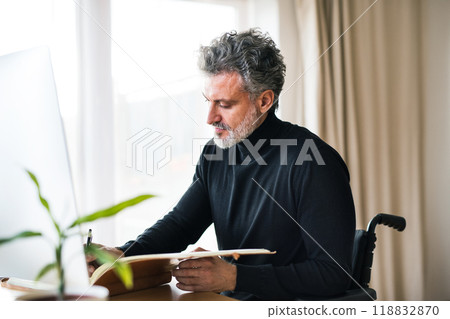 Handsome man in wheelchair working from home office, using computer in office. Telecommuting and home office. Handsome man in wheelchair working from home office, using computer in office. Telecommuting and home office. 118832870