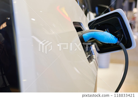 Close-up of electric vehicle charging at station. EV car with plugged-in cable recharging battery. Clean energy transportation 118833421