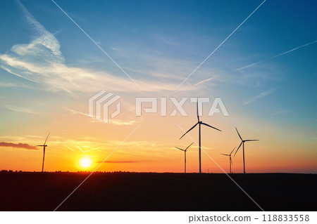 Silhouetted wind turbines in countryside landscape during sunset. Wind power plant generating clean energy. Concept of renewable and sustainable energy 118833558