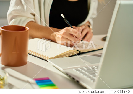 Person is sketching in notebook while working remotely at desk with laptop. Freelance work at home office. Graphic designer drawing sketch Person is sketching in notebook while working remotely at desk with laptop. Freelance work at home office. Graphic designer drawing sketch 118833580