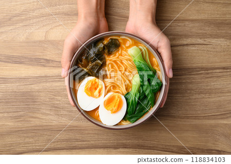 Spicy noodles soup with egg, seaweed and bok choy in bowl with hand, Asian noodles style 118834103