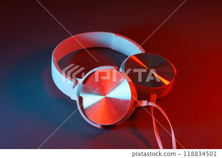 White, over-the-ear headphones with a wire on a colored, dark background. White, over-the-ear headphones with a wire on a colored, dark background. 118834501