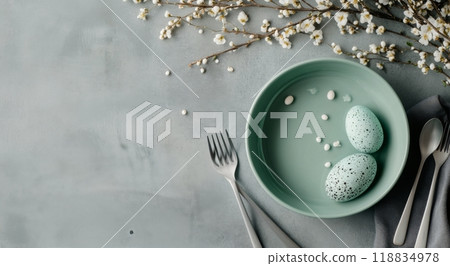 Decorative Easter eggs in a bowl surrounded by blossoms and utensils on a soft grey surface 118834978