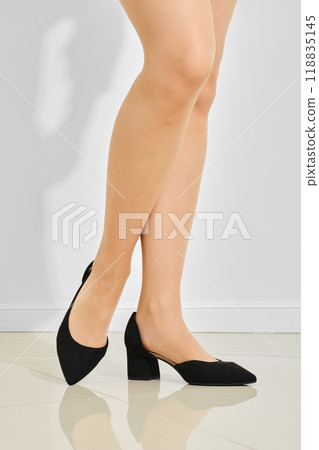 Close-up view of female legs wearing black suede high heels and beige tights. 118835145