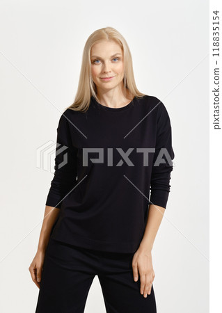 Elegant woman in a black outfit poses confidently against a plain backdrop 118835154