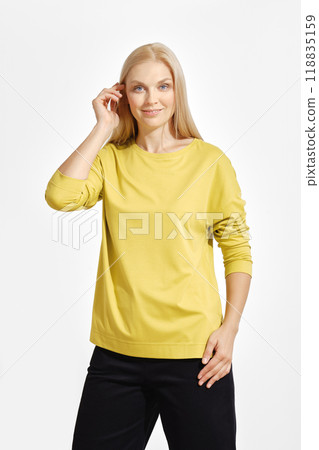 A woman poses confidently in a yellow long-sleeve top against a simple white background 118835159