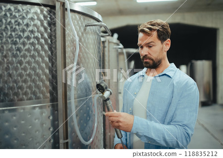 Winemaker standing in the wine cellar, controlling pressure in fermentation tank. Winemaker standing in the wine cellar, controlling pressure in fermentation tank. 118835212