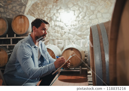 The winemaker standing in the wine cellar, monitoring the fermentation and aging processes in large barrels. 118835216