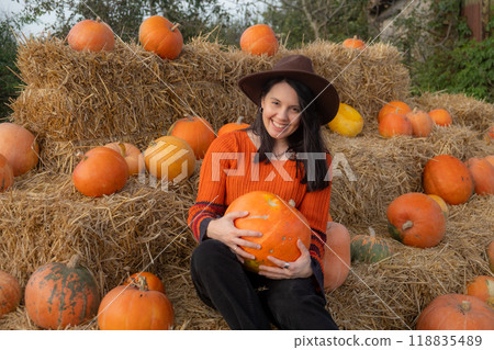 Woman holding a pumpkin sitting on hay bales Woman holding a pumpkin sitting on hay bales 118835489