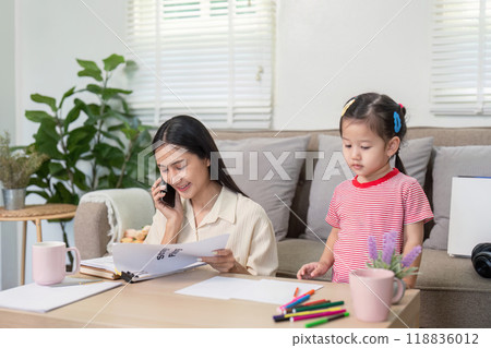 Focused Mother Balancing Professional Tasks While Daughter Observes 118836012