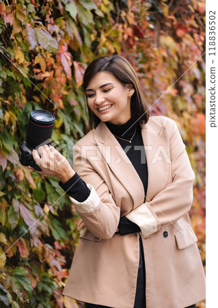 Happy smiled female photographer during her work. Stylish woman hold mirrorless camera. Autumn mood 118836502