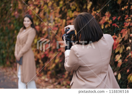 Back view of female photographer makes a photo for beautiful woman. Autumn mood Back view of female photographer makes a photo for beautiful woman. Autumn mood 118836516