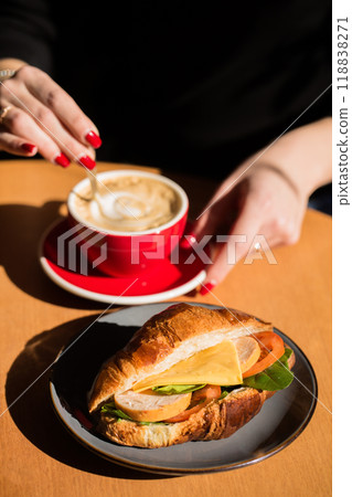 A woman drinks coffee with a croissant at a table A woman drinks coffee with a croissant at a table 118838271
