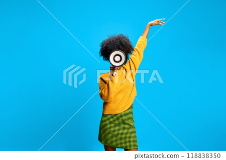 Woman shouting to megaphone, pointing to sky, inspiring confidence against bright blue studio background. 118838350