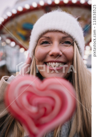 Portrait of young smiling woman holding heart shape lollipop in winter time outdoors. 118838525