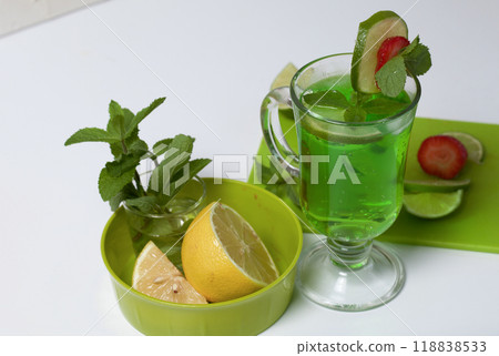 Green lemonade in a glass. Decorated with lime and strawberries. With sprigs of mint. Near lemon and mint. 118838533