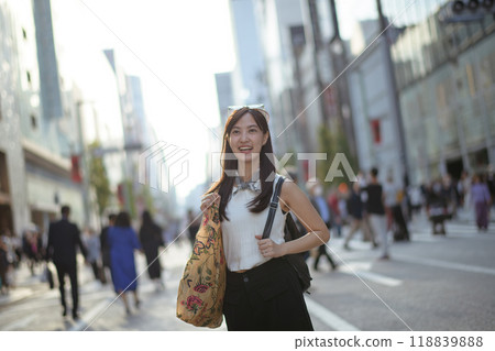 Asian woman in Tokyo's urban scene, standing at a road corner with a trendy tote bag, showcasing a perfect blend of casual life and modern tech use. Asian woman in Tokyo's urban scene, standing at a road corner with a trendy tote bag, showcasing a perfect blend of casual life and modern tech use. 118839888