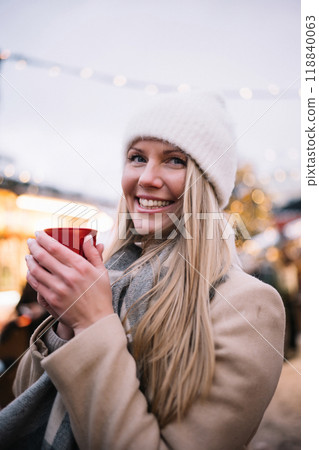 Young woman with long blonde hair enjoys hot drink at a festive outdoor market in winter Young woman with long blonde hair enjoys hot drink at a festive outdoor market in winter 118840063