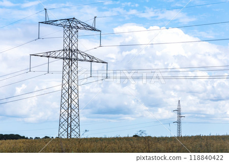 Electricity concept. High voltage power line pylons, electrical tower on a green field with blue sky. Electricity concept. High voltage power line pylons, electrical tower on a green field with blue sky. 118840422