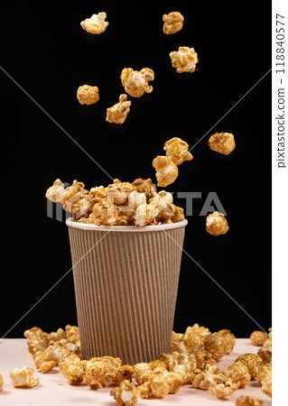 Sweet caramelized popcorn pouring into a glass on a black background. 118840577