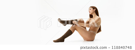 Banner. Adjusting socks, woman sits gracefully, combining casual comfort with elegance against white studio background with copy space. 118840748