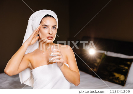 Young serene relaxed woman with bath towel drinking water after taking shower bath at home. Beauty treatment, hydration concept. 118841209