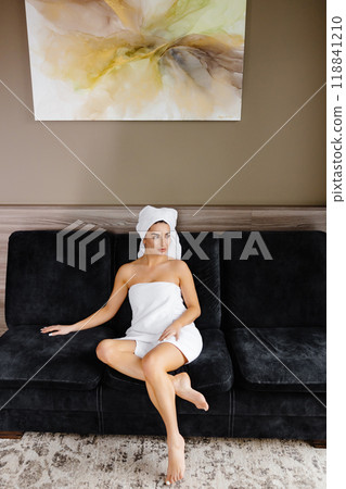 Happy beautiful woman wearing bathrobe and white towel with perfect complexion touching face looking at camera, sitting in room. Advertising of skin care spa wellness concept Happy beautiful woman wearing bathrobe and white towel with perfect complexion touching face looking at camera, sitting in room. Advertising of skin care spa wellness concept 118841210