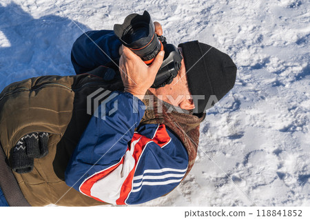 an elderly man with a camera in his hands is lying in the snow 118841852
