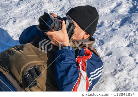 an elderly man with a camera in his hands is lying in the snow an elderly man with a camera in his hands is lying in the snow 118841854