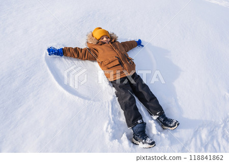 A boy lies in the snow and makes a snow angel A boy lies in the snow and makes a snow angel 118841862