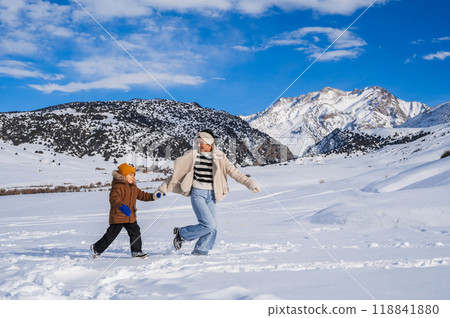 Mom and son running on a snow-covered slope against the backdrop of a mountain landscape in winter Mom and son running on a snow-covered slope against the backdrop of a mountain landscape in winter 118841880