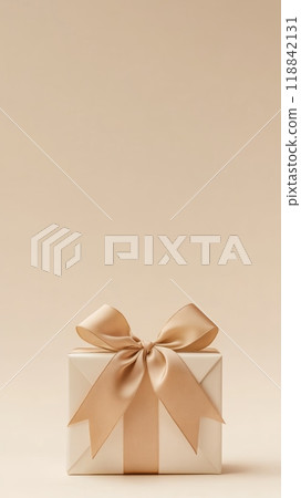 Golden gift box with a satin ribbon bow on a beige background. Perfect for Christmas, New Year's, or holiday gift concepts. 118842131