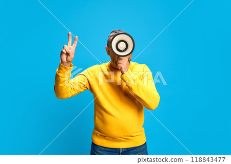 Man in yellow sweater, holding megaphone in hand, announcing holiday sale, seasonal discounts against blue studio background Man in yellow sweater, holding megaphone in hand, announcing holiday sale, seasonal discounts against blue studio background 118843477