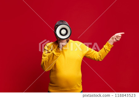 Man in bright yellow sweater talking in megaphone against red studio background. Holiday Sale Kickoff Man in bright yellow sweater talking in megaphone against red studio background. Holiday Sale Kickoff 118843523
