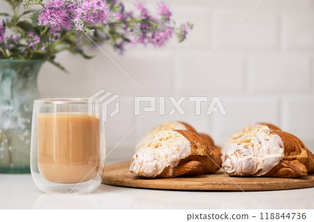 Delicious fresh croissants on wooden tray and glass of coffee on white table, closeup, tasty breakfast 118844736