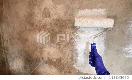 painting a plastered gray wall with a roller in white. wall repairs 118845623