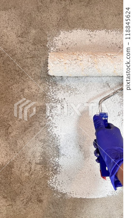 painting a plastered gray wall with a roller in white. wall repairs 118845624